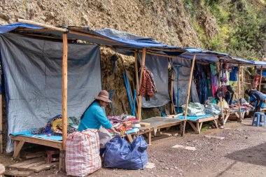 Pisac, Peru - 20 Mart 2025: Pisac arkeoloji sahasının girişinde dokuma tekstil hediyelik eşya satan yerli kadın