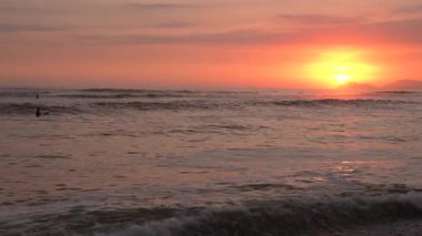 Sörfçü, Lima, Peru 'da gün batımında Pasifik okyanusu dalgalarında kürek çeker.