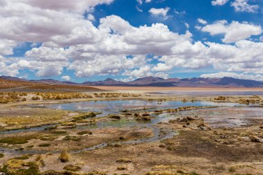 Sakin gölü ve Bolivya 'daki suya yansıyan kabarık bulutlarıyla nefes kesici dağ manzarası.