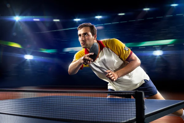 young sports man tennis player playing on black background with lights
