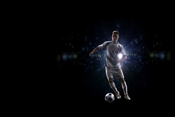 Jogador de futebol em ação sobre fundo preto — Fotografia de Stock