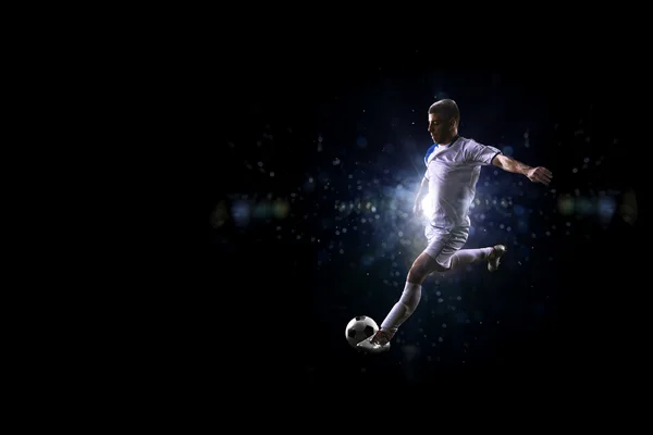 Jogador de futebol em ação sobre fundo preto — Fotografia de Stock