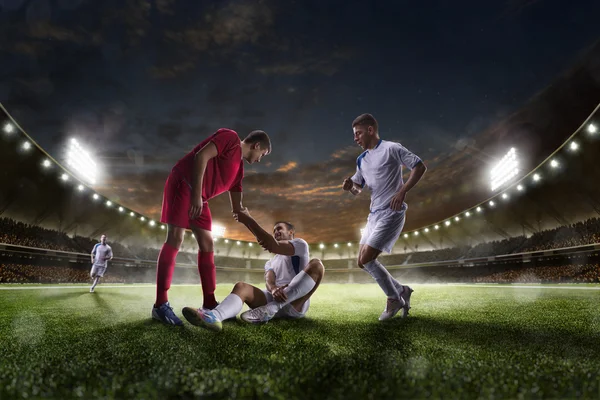 Joueur de football aide surl'autre sur le coucher du soleil panorama arrière-plan du stade — Photo