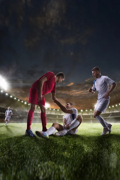 Jogador de futebol ajuda onother um no pôr do sol estádio panorama de fundo — Fotografia de Stock