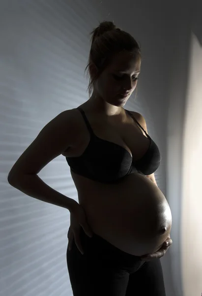 Pregnant woman touching stomach and leaning on window. — Stock Photo, Image