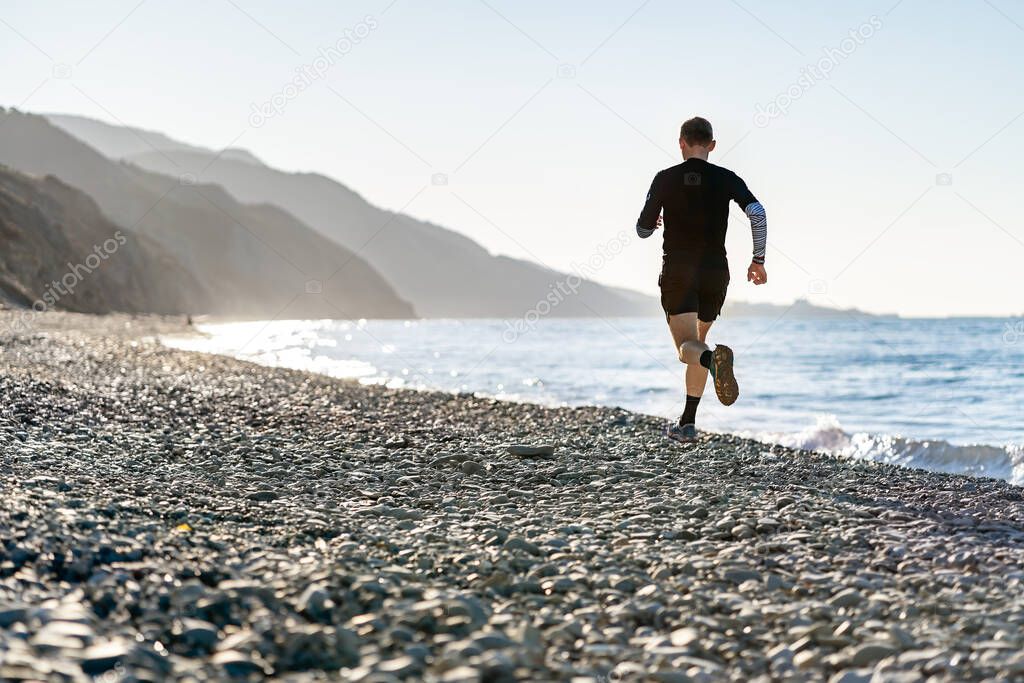 Man running on the beach, mountains background