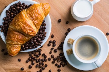 Kahvaltı kahve - Kupası, şeker, süt kabı ve kruvasan ahşap arka plan üzerinde kahve çekirdekleri ile.