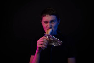 Boynunda oyun kulaklığı olan bir adam fast food yiyor. Sanal gerçeklik, oyunlar ve iletişim kavramı.