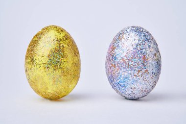 Beyaz arka planda altın ve gümüş renkli parlak yumurtalar.