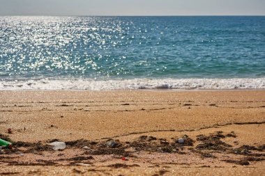 Plaja çöp döküldü. Kullanılmış kirli plastik şişeler, paketler ve diğer ev çöpleri..