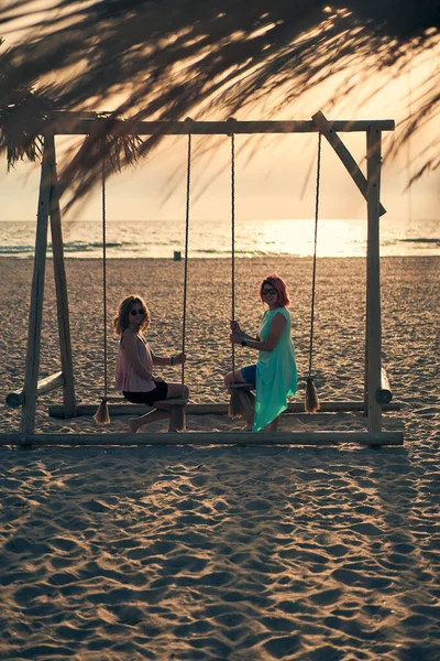 Duas jovens mulheres atraentes descansando no mar na praia ao pôr do sol. — Fotografia de Stock