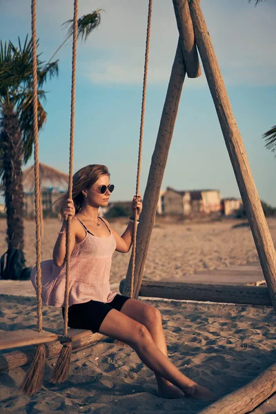 Joven mujer atractiva está descansando en el balancín en la playa al atardecer. — Foto de Stock