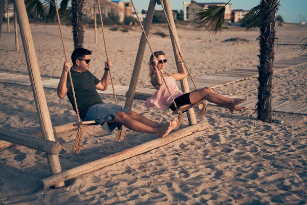 Joven pareja atractiva balanceándose en el balancín en la playa. — Foto de Stock