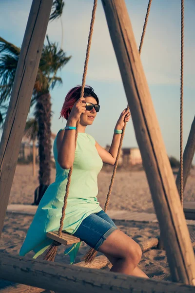 Jovem mulher atraente com cabelo rosa está descansando na beira-mar na praia ao pôr do sol. — Fotografia de Stock