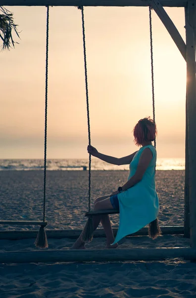 Mujer atractiva joven con el pelo rosa está descansando en balancín en la playa al atardecer. — Foto de Stock