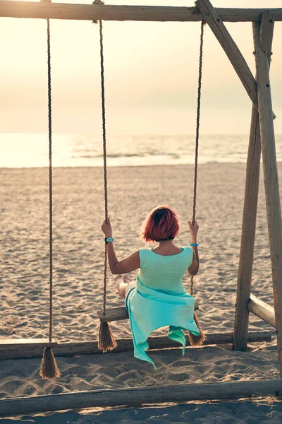 Mujer atractiva joven con el pelo rosa balanceándose en balancín en la playa. — Foto de Stock