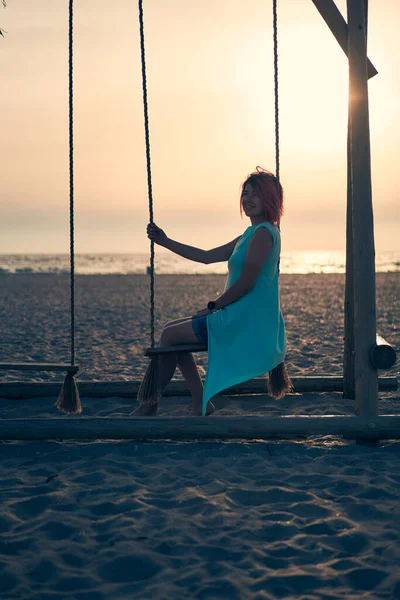 Mujer atractiva joven con el pelo rosa está descansando en balancín en la playa al atardecer. — Foto de Stock