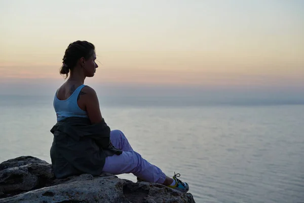 Frau sitzt auf einem Felsen, blickt auf die Meereslandschaft, den Sonnenuntergang und genießt die Aussicht und die frische Luft. — Stockfoto