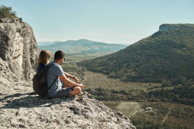 Çift bir kayanın üzerinde oturur, manzarayı seyreder ve manzaranın ve temiz havanın tadını çıkarır..