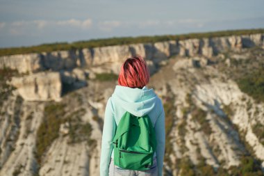 Genç bir kadın bir kayanın üzerinde kalır, manzaraya bakar ve manzaranın ve temiz havanın tadını çıkarır..