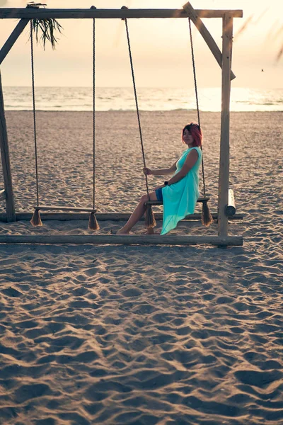 Mujer atractiva joven con el pelo rosa está descansando en balancín en la playa al atardecer. — Foto de Stock