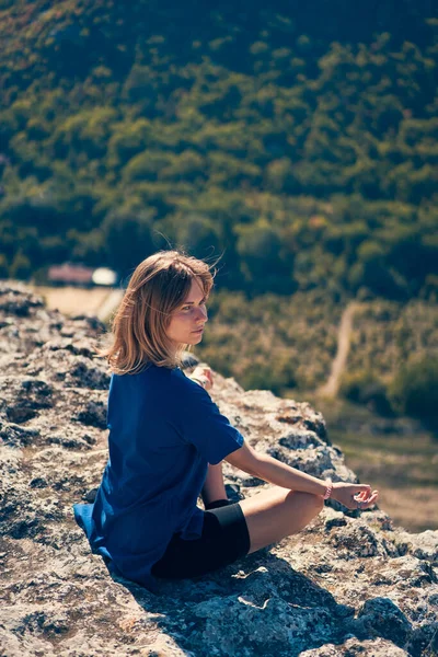 Jovem mulher senta-se em uma rocha, olhando para a paisagem e apreciando a vista e ar fresco. — Fotografia de Stock