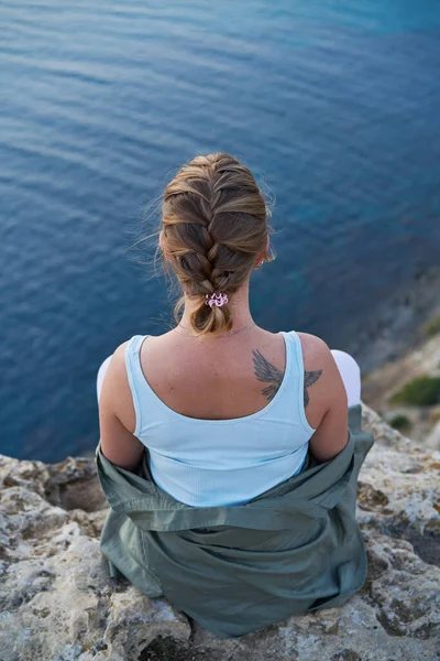 Mujer se encuentra en una roca, mirando el paisaje marino, puesta de sol y disfrutando de la vista y el aire fresco. — Foto de Stock