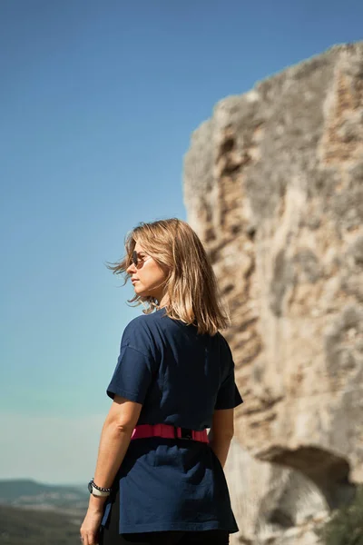 Jonge vrouw verblijven op een rots, kijken naar het landschap en genieten van het uitzicht en de frisse lucht. — Stockfoto