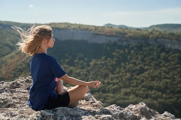 Jovem mulher senta-se em uma rocha, olhando para a paisagem e apreciando a vista e ar fresco. — Fotografia de Stock