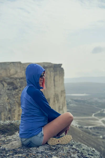 Mulher senta-se em uma rocha, olhando para a paisagem e apreciando a vista e ar fresco. — Fotografia de Stock