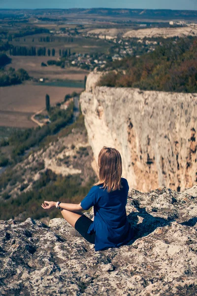 Jovem mulher senta-se em uma rocha, olhando para a paisagem e apreciando a vista e ar fresco. — Fotografia de Stock