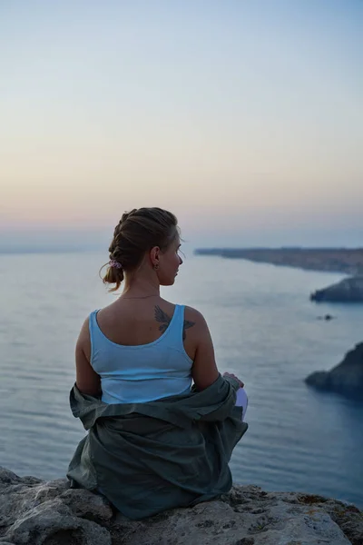 Mujer se encuentra en una roca, mirando el paisaje marino, puesta de sol y disfrutando de la vista y el aire fresco. — Foto de Stock