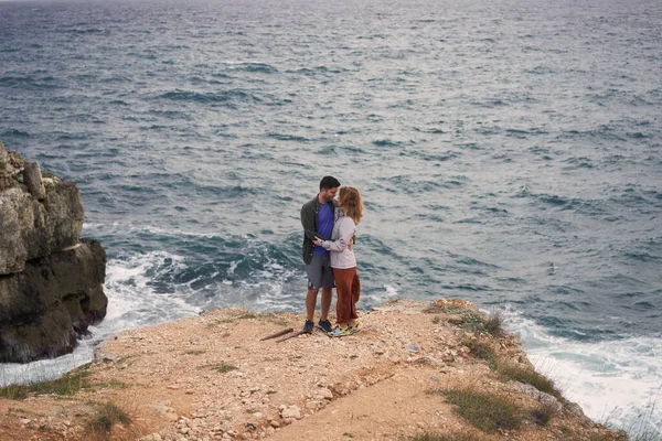 Pareja está de pie sobre una roca junto al mar, abrazándose, disfrutando de la vista y el aire fresco. —  Fotos de Stock