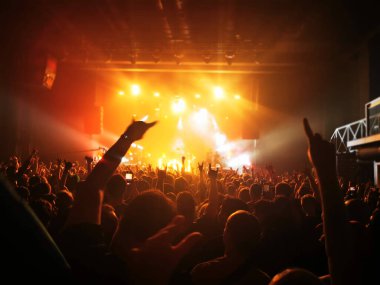Parlak sahne ışıkları önünde konser kalabalığının siluetleri