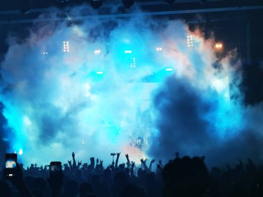 Parlak sahne ışıkları önünde konser kalabalığının siluetleri