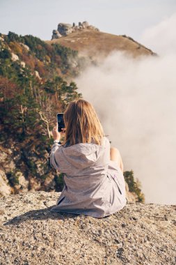 Kadın taşların üzerinde oturuyor, dinleniyor, fotoğraf çekiyor ve manzaranın ve temiz havanın tadını çıkarıyor..