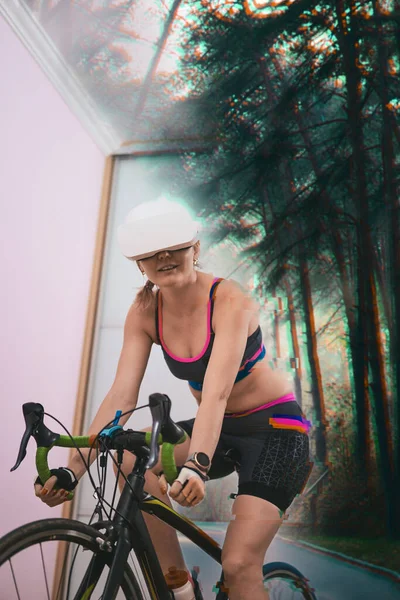 Woman trains at home on a stationary bike wearing VR-headset.