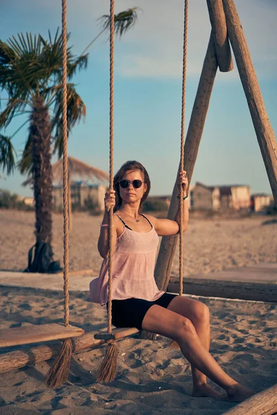 Joven mujer atractiva está descansando en el balancín en la playa al atardecer. — Foto de Stock