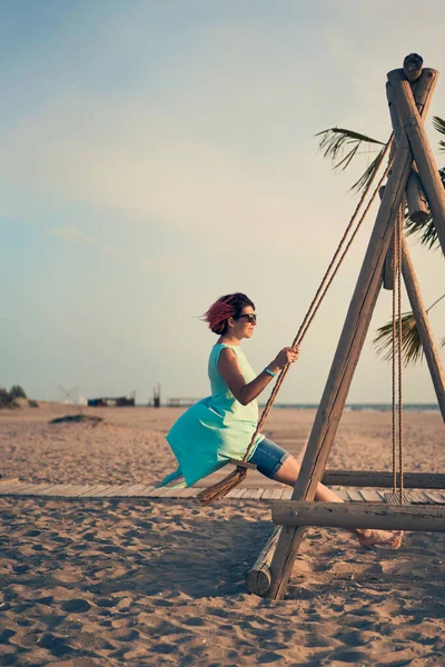 Mujer atractiva joven con el pelo rosa balanceándose en balancín en la playa. — Foto de Stock