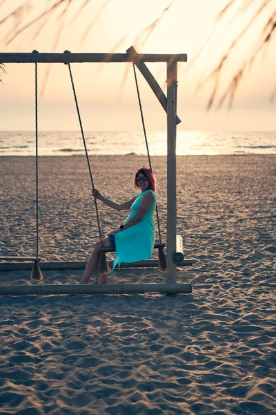 Mujer atractiva joven con el pelo rosa está descansando en balancín en la playa al atardecer. — Foto de Stock