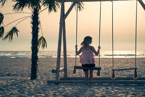 Joven mujer atractiva está descansando en el balancín en la playa al atardecer. — Foto de Stock