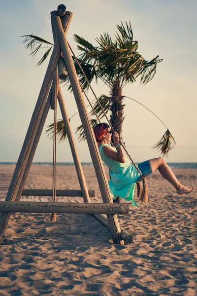 Mujer atractiva joven con el pelo rosa balanceándose en balancín en la playa. — Foto de Stock