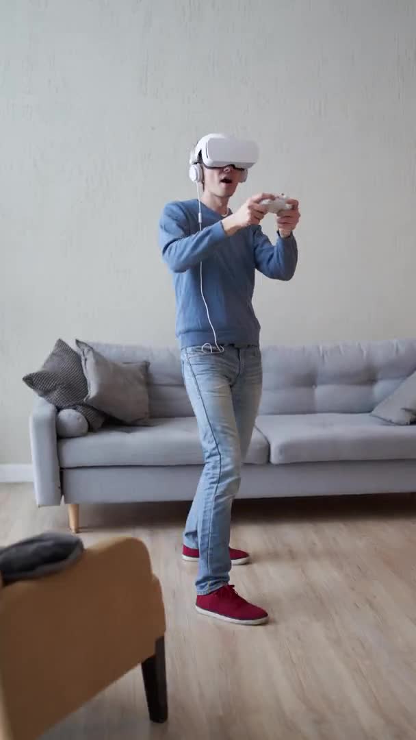 Человек играет в игру с гарнитурой виртуальной реальности и джойстиком. Вертикальное видео. — стоковое видео