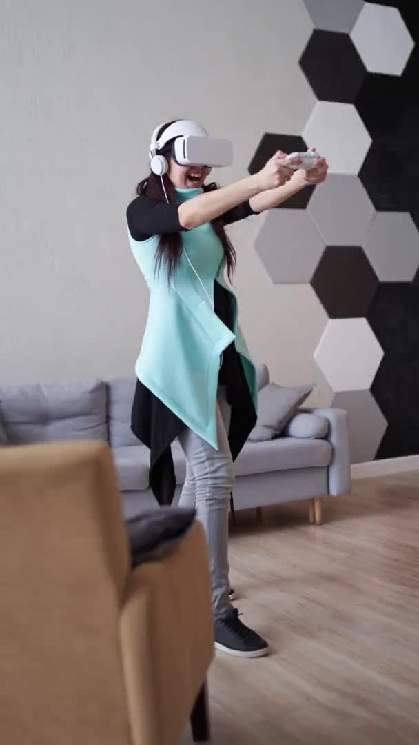 Женщина играет в игру с гарнитурой виртуальной реальности и джойстиком. Вертикальное видео. — стоковое видео