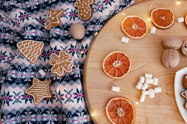 Strickpullover, Weihnachtsplätzchen, Girlanden, Marshmallows und getrocknete Orangen auf einem Holzkreis. Gemütliche Weihnachtskomposition — Stockfoto