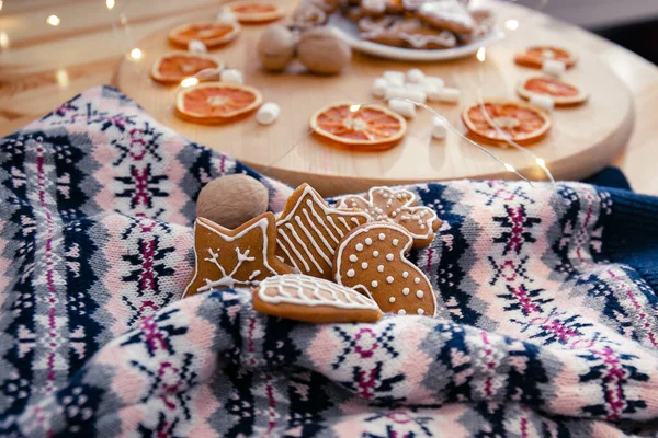 Weihnachtsplätzchen mit Zuckerguss liegen auf einem Strickpullover mit Ornament, Girlanden, Marshmallows und getrockneten Orangen auf einem Holzkreis. Gemütliche Neujahrskomposition — Stockfoto