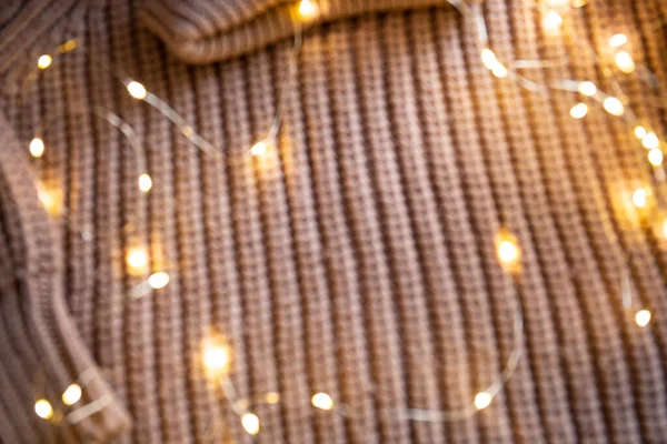 Luces de una guirnalda luminosa sobre un suéter de punto sobre la mesa. Fondo con enfoque suave. Concepto de Navidad. — Foto de Stock