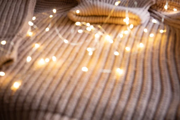 Luces de una guirnalda luminosa sobre un suéter de punto sobre la mesa. Fondo con enfoque suave. Concepto de Navidad. — Foto de Stock