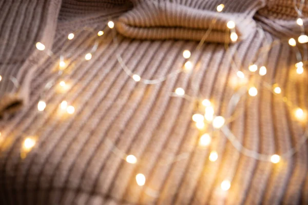 Lichter einer leuchtenden Girlande auf einem Strickpullover auf dem Tisch. Hintergrund mit weichem Fokus. Weihnachtskonzept. — Stockfoto