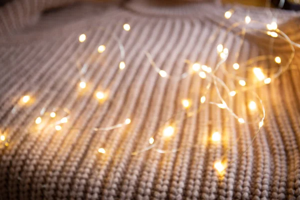 Lichter einer leuchtenden Girlande auf einem Strickpullover auf dem Tisch. Hintergrund mit weichem Fokus. Weihnachtskonzept. — Stockfoto